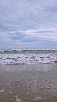 Vertical video of ocean waves crashing on the beach during a cloudy day