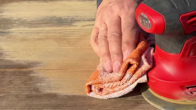Hand wiping fine wood dust from sanded old wooden table with cloth, cleaning wood surface after orbital sanding, preparing furniture for refinishing, DIY restoration at home.