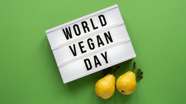 World Vegan Day lightbox sign with fresh yellow pears on a green background with copy space