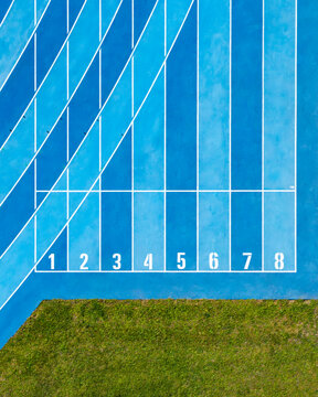 Aerial view of a blue running track with lanes numbered one through eight and adjacent green grass in Plock, Masovian Voivodeship, Poland.