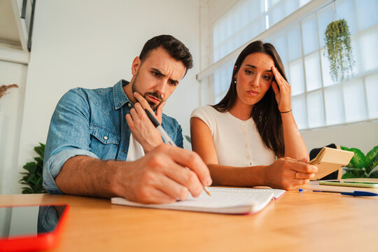 A thoughtful pair collaborates over a desk, jotting ideas on paper while consulting a notebook and taking turns discussing plans with calm focus. The scene shows teamwork focus and careful note taking