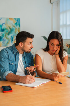 A focused pair sits at a wooden table as one writes in a notebook while the other gestures and speaks, conveying collaborative problem solving and shared decision making with calm concentration now