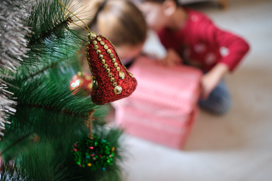Christmas bell ornament hanging on tree with children opening gifts