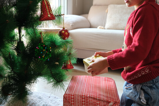 An unrecognisable child opening a Christmas present under a decorated tree