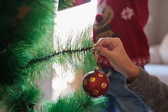 Child's hand hanging red christmas ornament on tree