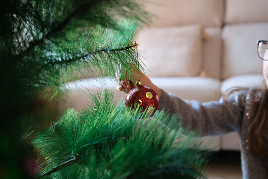 an unrecognizable girl decorating a Christmas tree with a red bauble