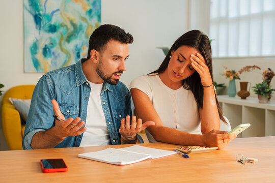 A couple sits at a wooden table studying papers and a tablet, engaged in a focused financial planning discussion. Ink, calculator, and notes hint at budgeting and decision making in a domestic