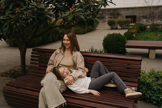 Mom sits on a bench while daughter lays on her lap in a park during daytime