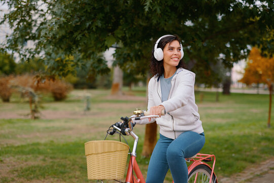 Woman smiling and wearing headphones, enjoying a peaceful bike ride in an autumn park, embracing a healthy outdoor lifestyle and leisure activity