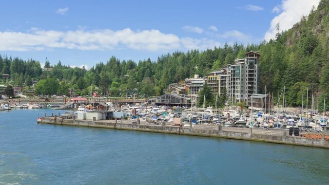 Boats docked at marina with forested hills and waterfront buildings on Bowen Island