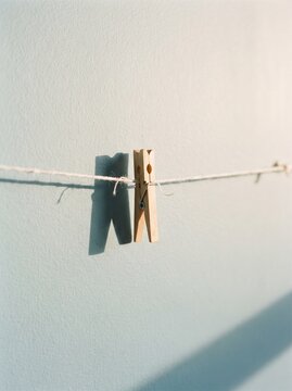 Single wooden clothes peg hanging on rope clothesline with shadow on wall, laundry clothespin concept