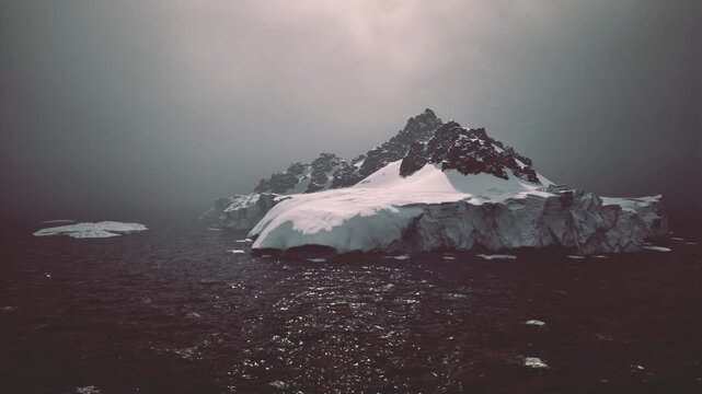 retreating ice with warming sea, scattered white floes and dark water glinting under muted sky, conveying climate shift and exposed rocky bed beneath thinning