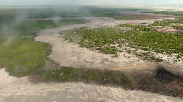 Aerial view over the Mababe Depression in Botswana, showing green mopane forest, open sandy ancient lakebed plains, marshes and water channels of the Khwai-Mababe system during a sandstorm.