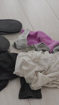 Person mops light colored wooden floor around scattered laundry including socks and fabric pieces. Feet are visible as mop moves across scene emphasizing household tidying