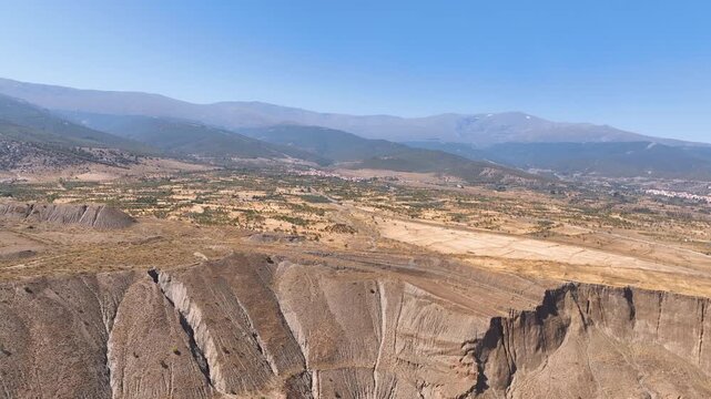 Aerial glides above heavily eroded hillsides, and towards sparse orchards looking further to the bush covered hills of Sierra Nevada Granada Province Spain