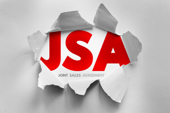 JSA means joint sales agreement. Text visible through a hole in grey paper. Collaborative partnership concept for companies joining forces to increase market reach and sales volume levels