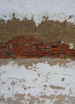 Deteriorating multilayer wall surface with chipped white paint and exposed concrete in a vertical composition, revealing weathered red clay brick, cracked mortar, and white mineral deposits
