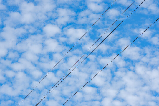 Three power cables crossing a sky of small scattered clouds