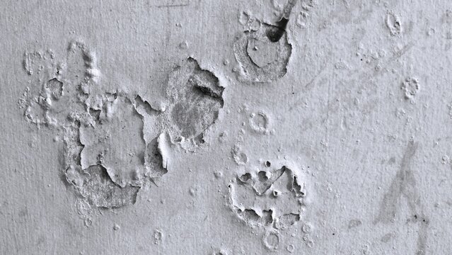 Black and white distressed wall showing peeling paint, exposed concrete, rough plaster and scattered imperfections, creating a raw vintage texture background.