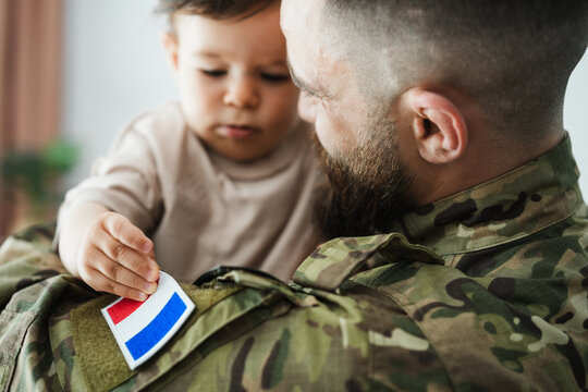 Male french soldier in military uniform hugs his little son at home while baby boy touching french flag - Emotional military happy homecoming concept - Main focus on man beard - UGC content