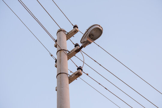 Concrete utility pole equipped with a street light lantern and overhead electrical power lines against a clear blue sky