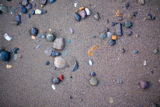 Flat lay texture of wet colorful pebbles and tiny sea shells scattered over coarse natural sand on a tranquil coastline