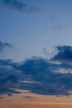 Vertical shot of peaceful evening sky featuring scattered blue clouds and soft orange sunset glow along horizon