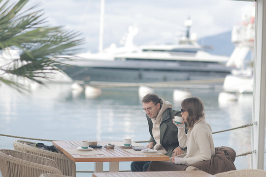 Couple Enjoying Coffee at Waterfront Cafe with Yacht in Background