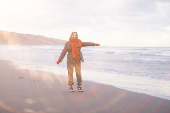Joyful Woman in Orange Headscarf Enjoying Serene Beach at Sunset