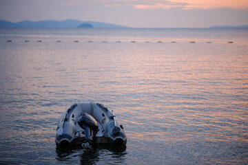 Inflatable zodiac dinghy boat equipped with Yamaha outboard motor floating on calm sea water at sunset with scenic horizon © Bugra Kaan Ersoy