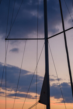 Sailboat mast with cross spreaders and rigging against a colorful sunset sky with warm orange twilight glow on the horizon