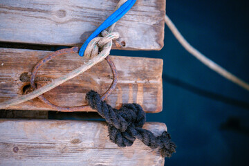 Fototapeta premium Rusty metal mooring ring on aged wooden pier boards with tied ropes and nautical knots over calm blue ocean water surface