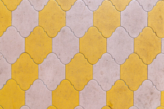 Interlocking yellow and beige tiles forming repeating pavement pattern