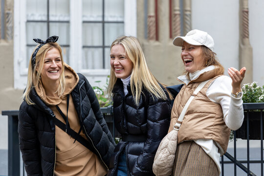 Cheerful friends laugh together on autumn city walk, sharing hugs and joyful travel moments. Candid group portrait captures friendship, reunion, happiness, leisure and weekend adventure outdoors