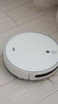 Round robot vacuum moving smoothly over wooden flooring. device top surface features illuminated control icons and sensors as it navigates floor demonstrating automated household appliance