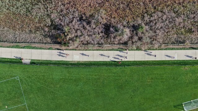 Aerial view of people walking and jogging along a paved path in a park with green grass and dry vegetation in Boulder, Colorado, United States.