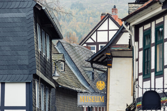 Scenic Goslar rooftops frame historic street with half timbered houses, slate facades and museum sign. Soft autumn tones and hazy hills create tranquil heritage mood in charming old town center