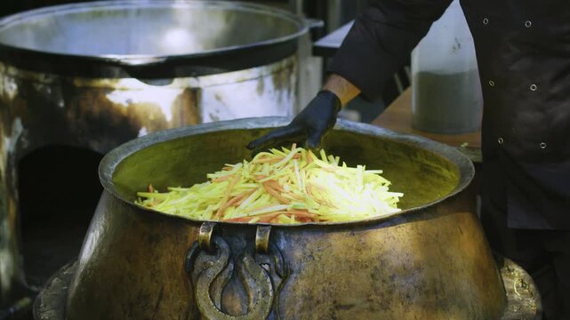 Close-Up of Chef Hand in Black Glove Spreading Sliced Carrots in Large Cauldron for Pilaf