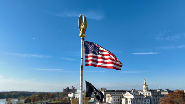 Aerial view of the American flag and POW MIA flag flying on a pole with the New Jersey State House dome in the background in Trenton, New Jersey, United States.