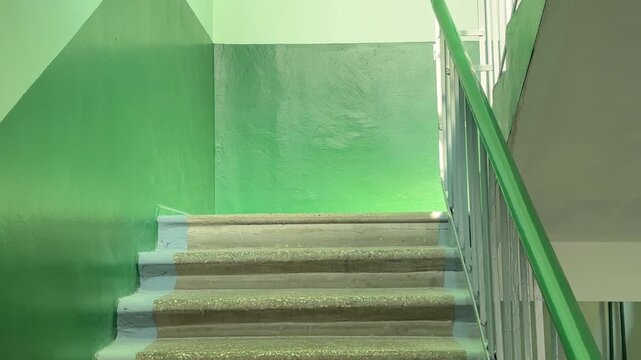 Empty green stairwell with concrete steps and metal handrail inside a residential building