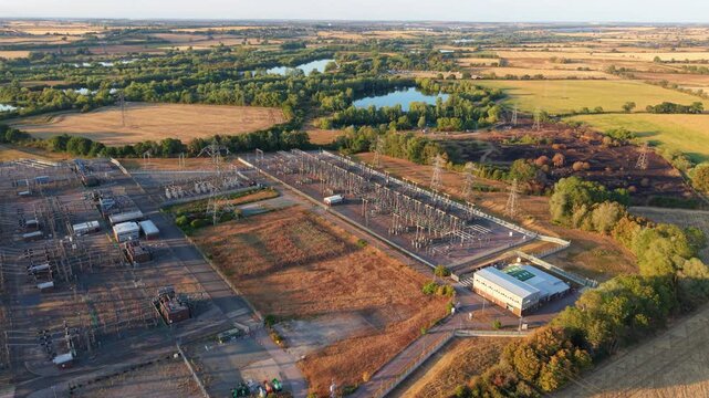 Aerial view of Grendon national grid station 400kV with electrical transformers and pylons surrounded by rural fields and lakes in Northampton, England, United Kingdom.