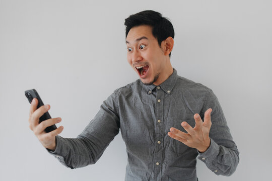 Asian man surprised by smartphone content, mouth open and eyes wide.