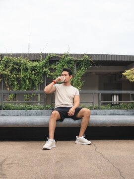 Young Asian man in casual sportswear drinking water during a break on a city rooftop.