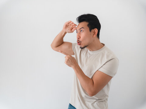 Curious young Asian man shielding his eyes and pointing, observing something interesting.