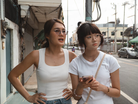 Two young Asian women exploring a bustling city street, looking around with curious expressions.