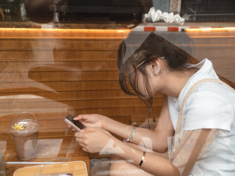 Casual moment of a young Asian woman browsing her smartphone in a cozy cafe setting.