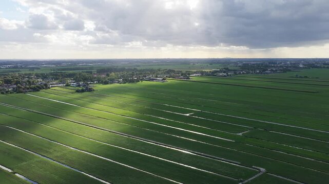 Aerial drone view of polders and agricultural fields in the Netherlands. Rural landscape with canals and cloud shadows under a blue sky.

