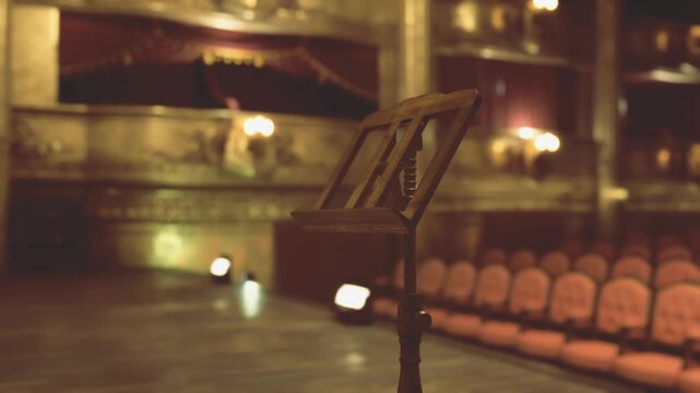 Gilded stage with antique music stand, baroque ornamentation and crystal chandelier glow, plush red seats and proscenium arch create warm nostalgic atmosphere