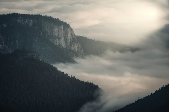 Dramatic mountain cliff rising above a sea of clouds with misty valleys and soft sunlight, cinematic nature landscape