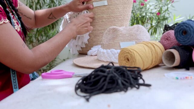 Woman's hands weaving a macrame decoration on a straw bag